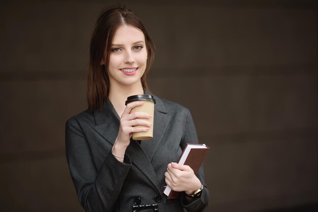 Jonge vrouw in een pak met een notitieboekje en koffie op straat kijkt in het frame