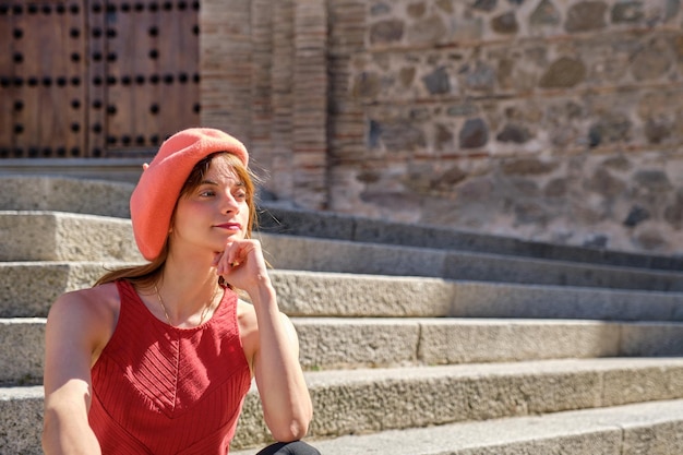 Jonge vrouw in een rode jurk, zittend op een stenen trap, rustend in de zon tijdens het bezoeken van bezienswaardigheden