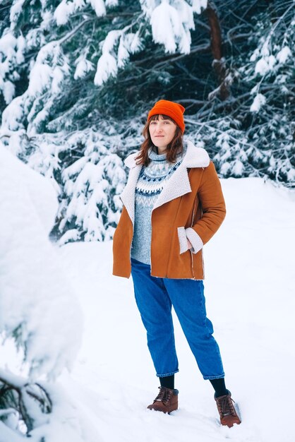 Jonge vrouw in een rode warme muts en jas op een achtergrond van besneeuwd bos