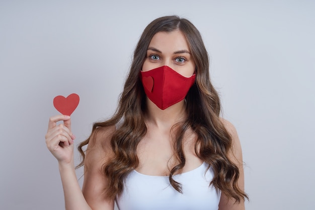 Jonge vrouw in een rood beschermend masker, met een hart van papier in haar hand