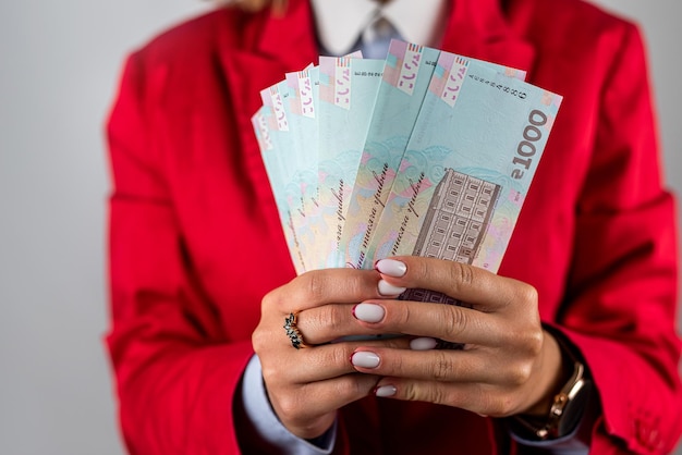 Foto jonge vrouw in een rood jasje met een stapel geld in dollars geïsoleerd op een effen achtergrond