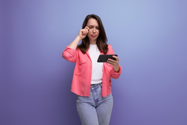 Jonge vrouw in een roze shirt en spijkerbroek communiceert op een mobiele telefoon op een studio geïsoleerde achtergrond