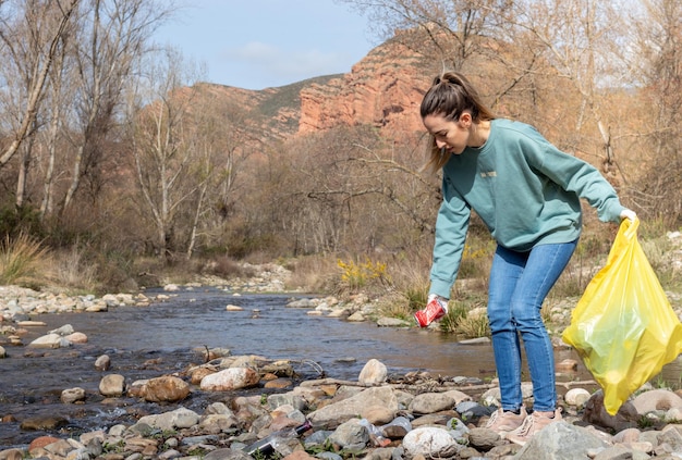 Foto jonge vrouw in een vuilnisophaaldienst die een blikje ophaalt bij de rivier