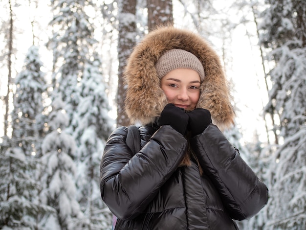 Jonge vrouw in een winterdonsjack met bontkap loopt in de winter door het bos