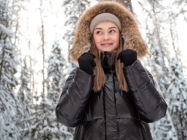 Jonge vrouw in een winterdonsjack met bontkap loopt in de winter door het bos