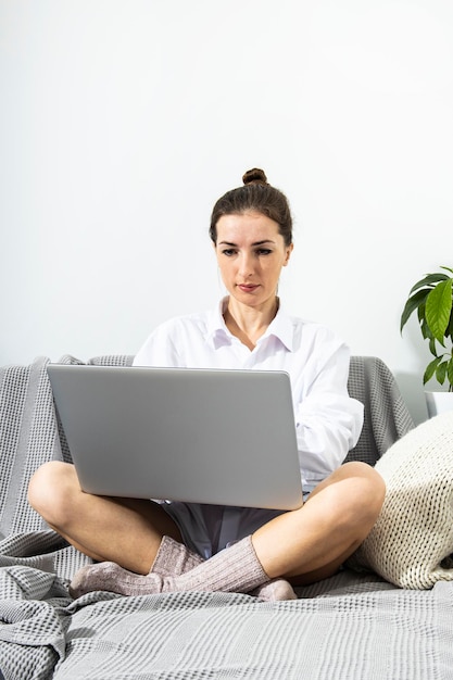 Jonge vrouw in een wit overhemd werkt achter een laptop op een bank