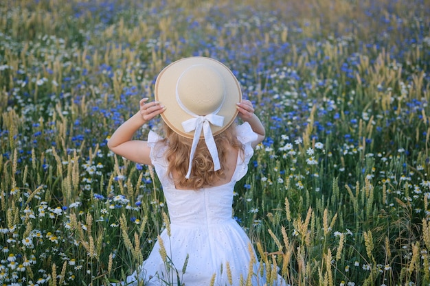 Jonge vrouw in een witte jurk en vintage hoed in een weiland met prachtige wilde bloemen