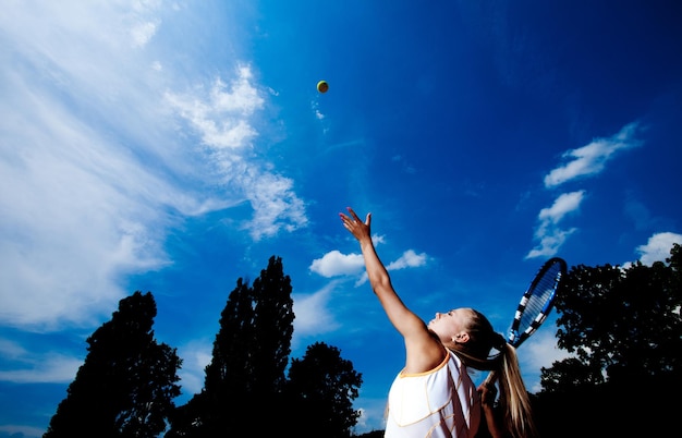 Jonge vrouw in een witte tennisjurk die balservice ontwikkelt