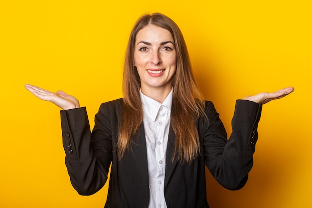 Jonge vrouw in een zwarte jas maakt een presentatie, houdt haar handpalmen op een gele.