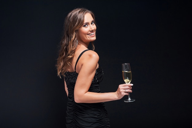 Jonge vrouw in elegante kleding die met glas champagne tegen zwarte blijft