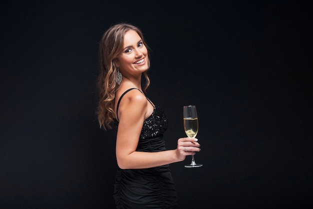 Jonge vrouw in elegante kleding die met glas champagne tegen zwarte blijft