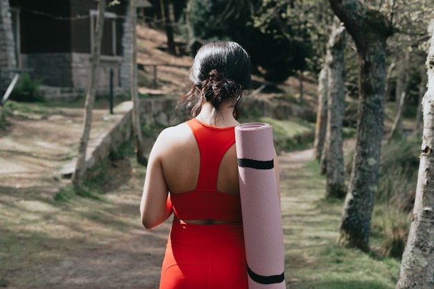 Jonge vrouw in fitness kleding glimlachen naar de camera in het park met een yoga mat en een fles water