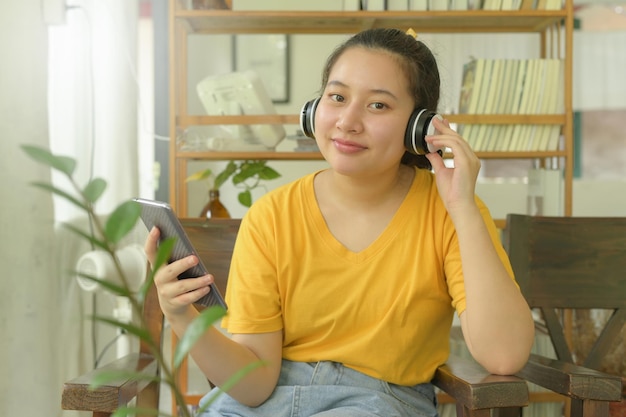 Jonge vrouw in geel shirt luisteren naar muziek van smartphone-app thuis