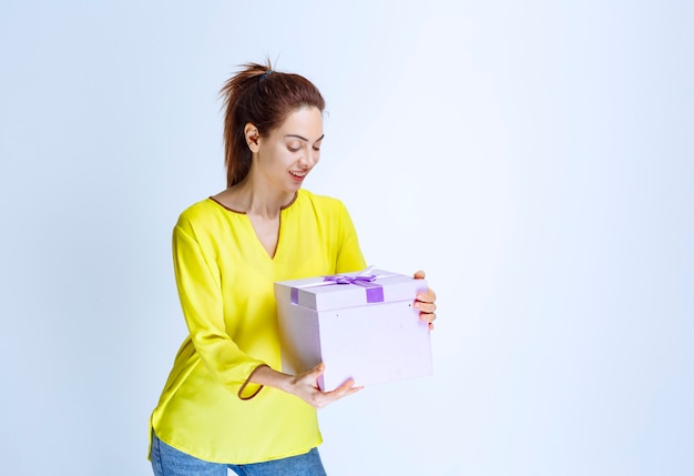 Jonge vrouw in geel shirt met een paarse geschenkdoos en ziet er gelukkig uit