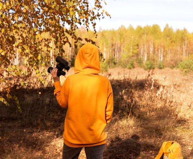 Jonge vrouw in gele hoodie met verrekijker in herfstbos Birdwatching ecology Research