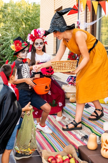 Jonge vrouw in gele jurk en zwarte heksenhoed die buigt voor een groep griezelige halloween-kinderen