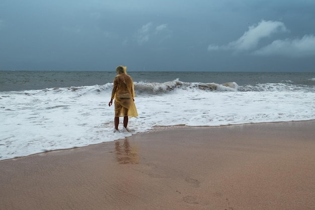 Jonge vrouw in gele regenjas op het strand in zware regen in Bali