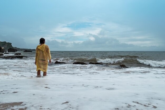 Jonge vrouw in gele regenjas op het strand in zware regen in Bali