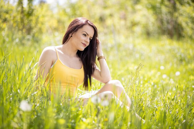 Foto jonge vrouw in gele top die in de zomer in het gras zit