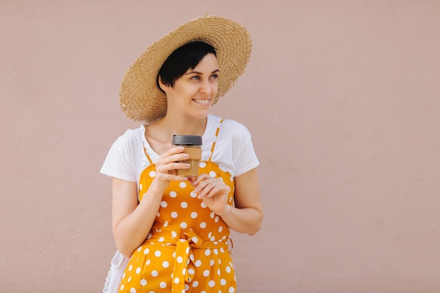 Jonge vrouw in gele zomerkleren met een Eco-zak fruit en herbruikbare koffiemok.