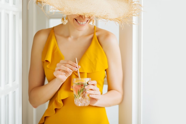 Jonge vrouw in gele zwembroek en strohoed met een cocktail close-up