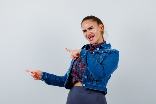 Jonge vrouw in geruit overhemd, spijkerjasje wijzend naar de zijkant, zijwaarts staand en vrolijk kijkend.