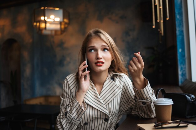 Jonge vrouw in gestreepte trenchcoat zorgvuldig praten over mobiel