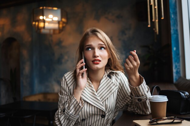 Jonge vrouw in gestreepte trenchcoat zorgvuldig praten over mobiel