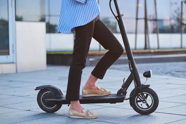 Jonge vrouw in gestripte blazer rijdt op haar nieuwe elektrische scooter op straat.