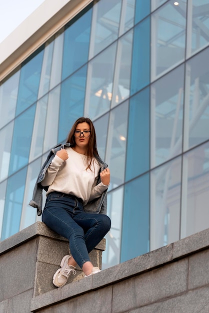 Jonge vrouw in glas op straat zonnige dag in de stad Stijlvolle jonge vrouw naast modern gebouw Verticaal frame