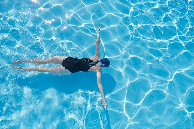 Jonge vrouw in GLB-sportenzwempak zwemmen onderwater in blauw openluchtzwembad