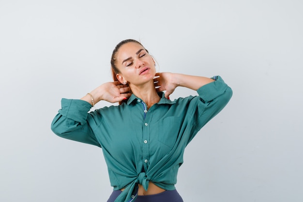 Jonge vrouw in groen shirt die lijdt aan nekpijn en er moe uitziet, vooraanzicht.