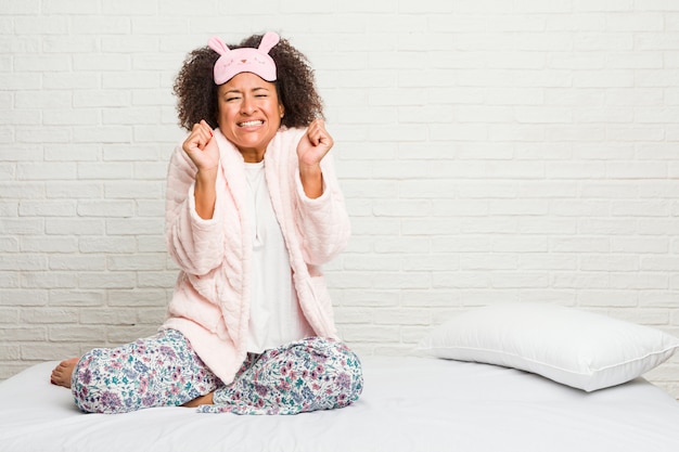 Jonge vrouw in het bed dat pijama draagt die vuist opheft, gelukkig en succesvol voelt. Overwinning concept.