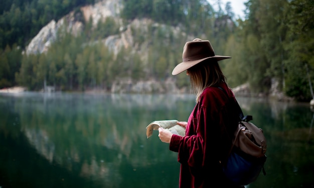 Jonge vrouw in hoed en rood shirt met kaart in de buurt van het meer