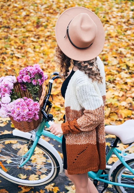 Jonge vrouw in hoed met blauwe fiets en boeketbloemen