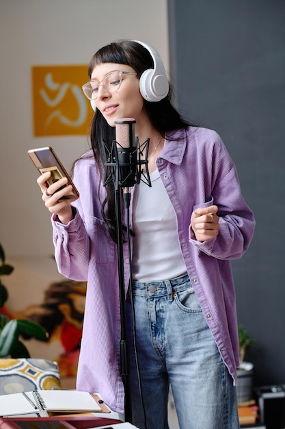 Jonge vrouw in hoofdtelefoons die haar smartphone gebruiken om lied in microfoon te zingen