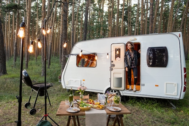 Foto jonge vrouw in huis op wielen tussen dennenbomen en geserveerd tafel vooraan