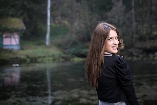 jonge vrouw in jas die achter haar schouder kijkt en lacht naar het meer