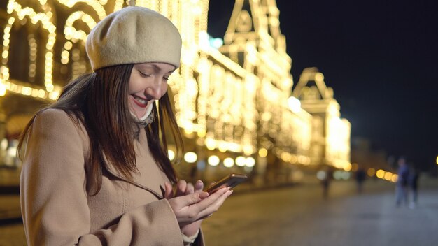 Jonge vrouw in jas staat niet vierkant met telefoon.