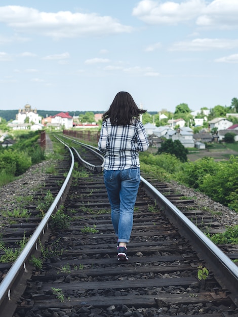 Jonge vrouw in jeans en shirt loopt langs het spoor