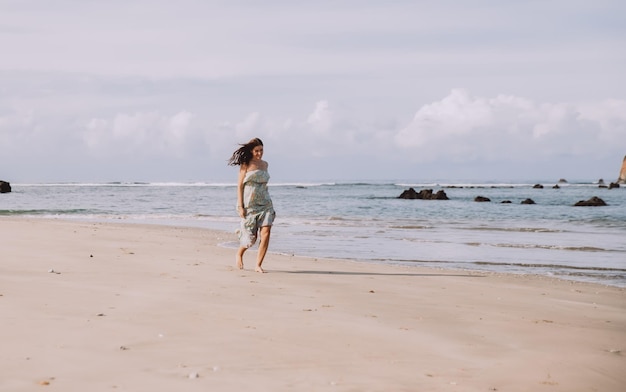 Jonge vrouw in jurk alleen wandelen op het strand in tropische natuur. Vrije tijd