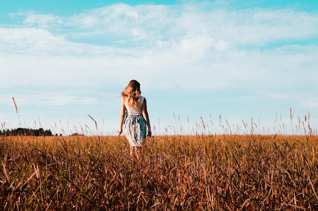 Jonge vrouw in jurk die langs een graanveld loopt