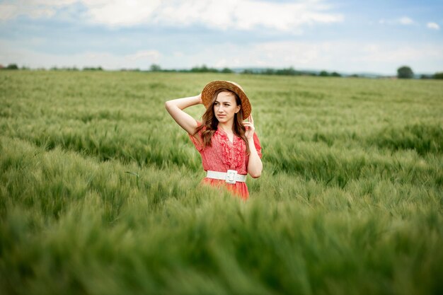 Jonge vrouw in jurk en hoed op groen gebied van gerst op het platteland. Stijlvol meisje in rustieke jurk genieten van rustig moment in gras in de zomer. Rustig landelijk moment