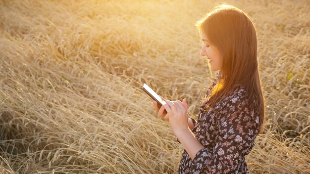 Jonge vrouw in jurk kijkt naar de telefoon terwijl ze in een tarweveld staat copyspace