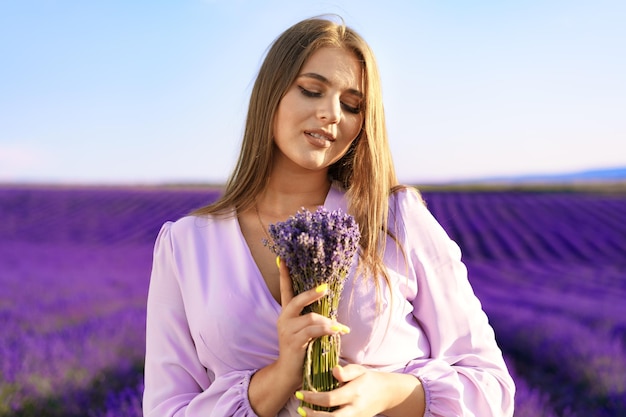 Jonge vrouw in jurk met boeket bloemen in lavendelveld