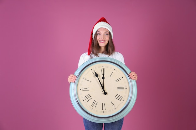 Jonge vrouw in kerstmuts met klok op kleur achtergrond. Kerst aftellen concept