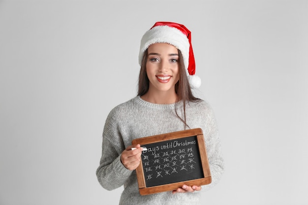 Jonge vrouw in kerstmuts met schoolbord dagen tellen tot Kerstmis, op lichte achtergrond