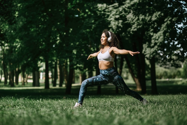 Jonge vrouw in koptelefoon die fitnessoefeningen uitvoert in de pa