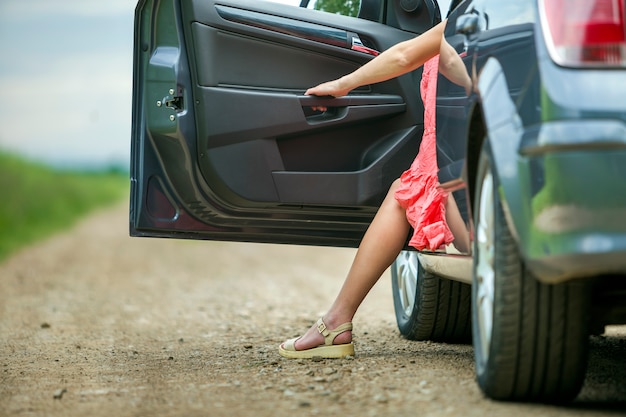 Jonge vrouw in korte jurk die auto met open deur op zonnige vage landelijke weg weggaat