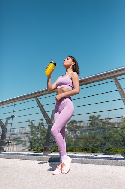 Jonge vrouw in montage sport slijtage op brug op warme zonnige ochtend met fles water shaker dorstig na training moe drinken